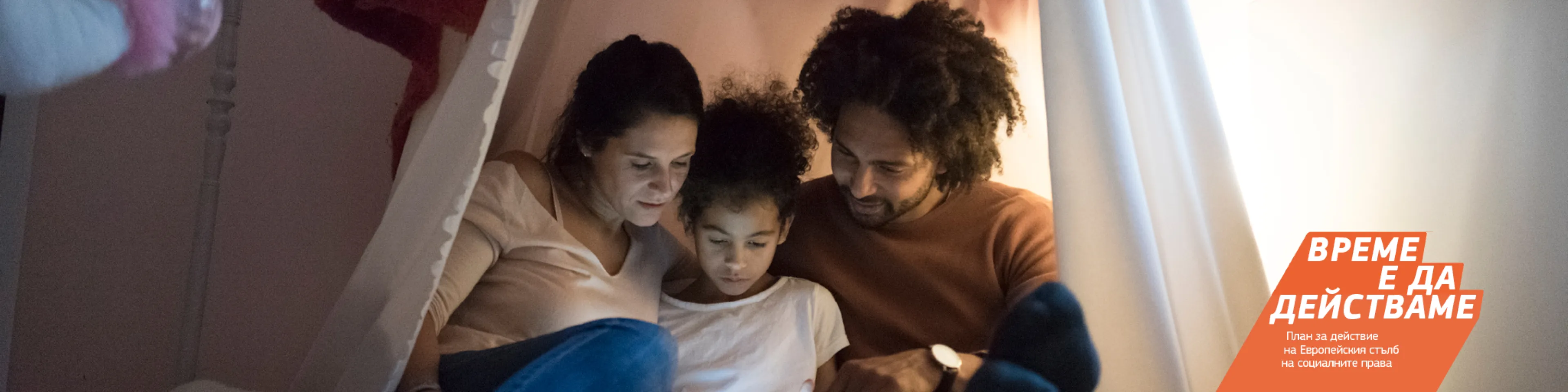 Млади родители прекарват време с детето си, седнали близо един до друг под импровизирана палатка в спалнята на детето.