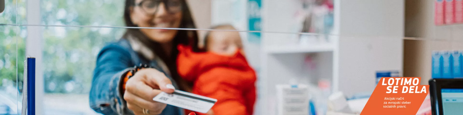 Kvinna med ett barn i famnen betalar med kort på ett apotek