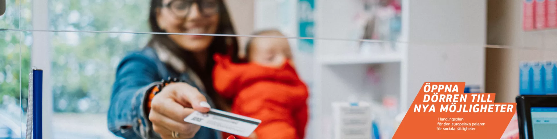 Kvinna med ett barn i famnen betalar med kort på ett apotek